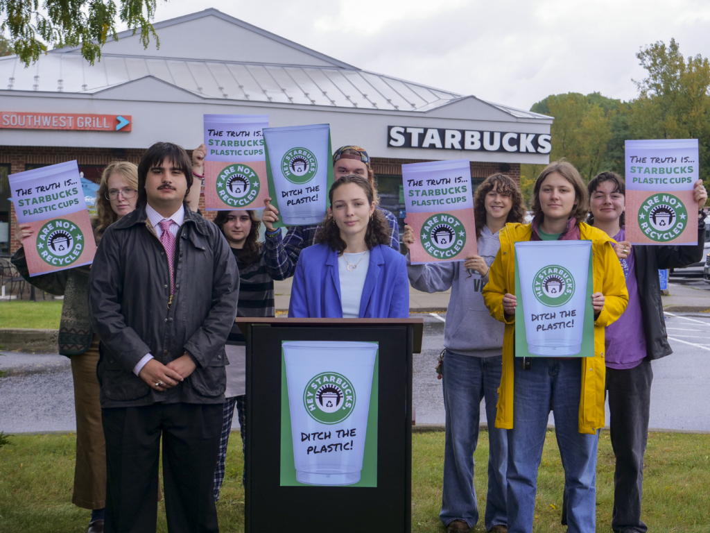 The VPIRG Environmental Health team standing around a podium with signs protesting Starbucks' plastic cup recycling claims, in front of a Starbucks